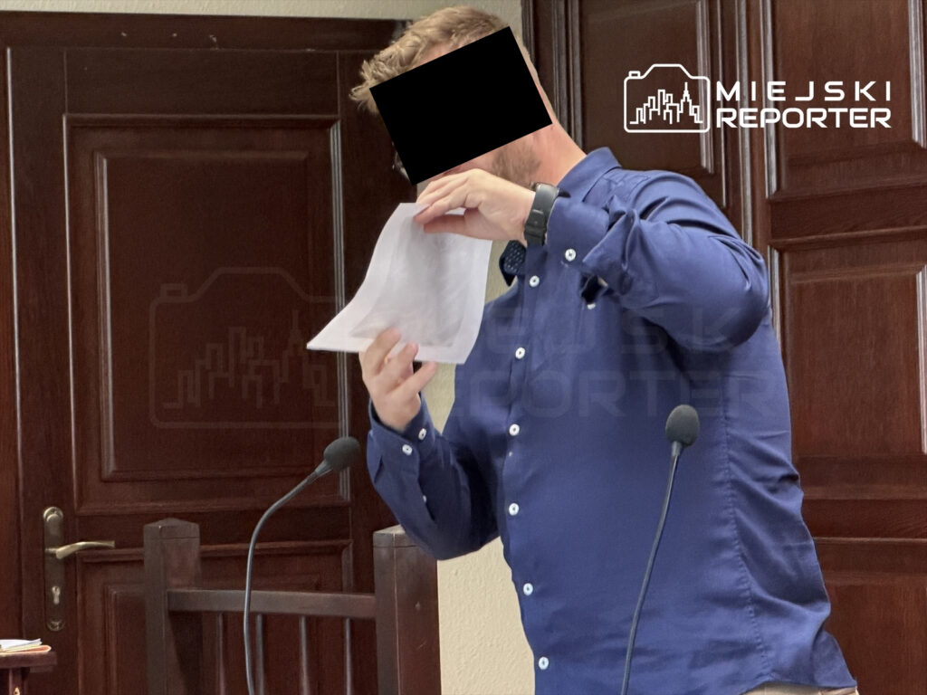 Mężczyzna w niebieskiej koszuli prezentuje dokument podczas rozprawy sądowej w sali sądowej z drewnianymi elementami.