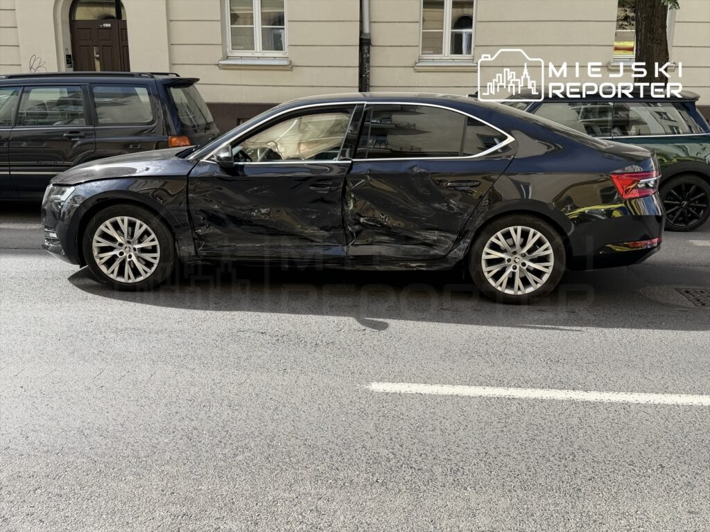 Czarny samochód osobowy z widocznymi uszkodzeniami na bocznej części stoi na ulicy.