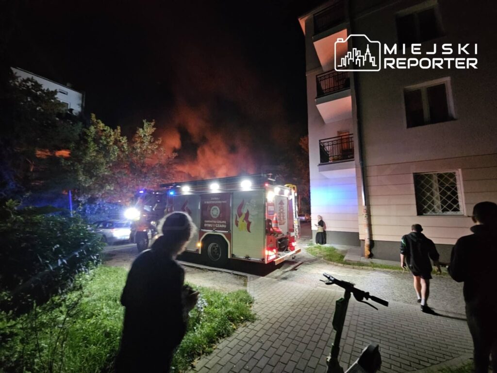 Straż pożarna z włączonymi sygnałami świetlnymi podjeżdża do miejsca pożaru w pobliżu budynku mieszkalnego.