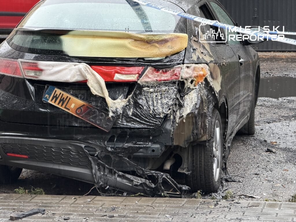Uszkodzony samochód osobowy z popaloną karoserią stoi na mokrej nawierzchni, obok taśma zabezpieczająca.
