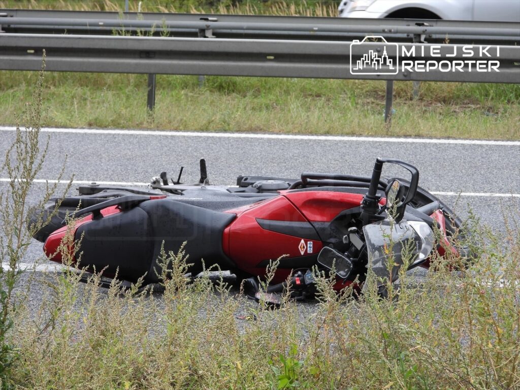 Motocykl leżący na poboczu drogi, otoczony trawą, z widocznymi uszkodzeniami.