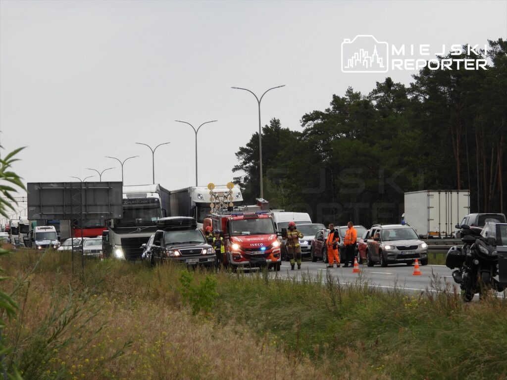 Ruch drogowy zablokowany przez służby ratunkowe i pojazdy na drodze ekspresowej, w tle widać ciężarówki i motocykle.