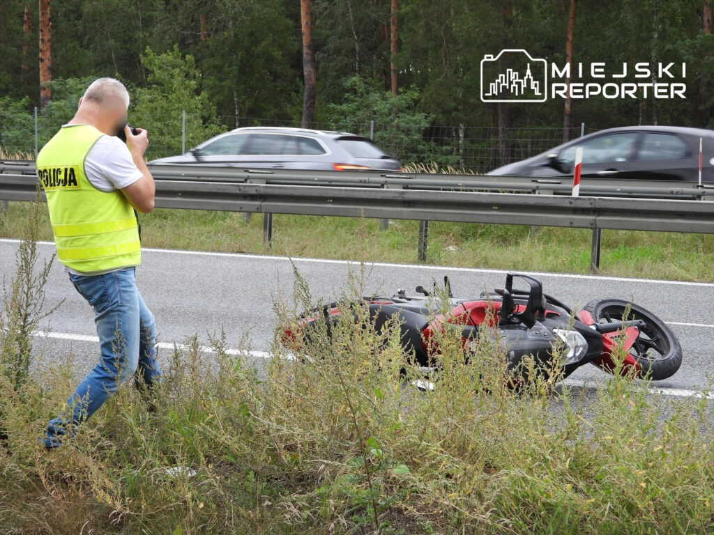 Policjant w kamizelce odblaskowej dokumentuje wypadek motocykli na poboczu drogi ekspresowej.