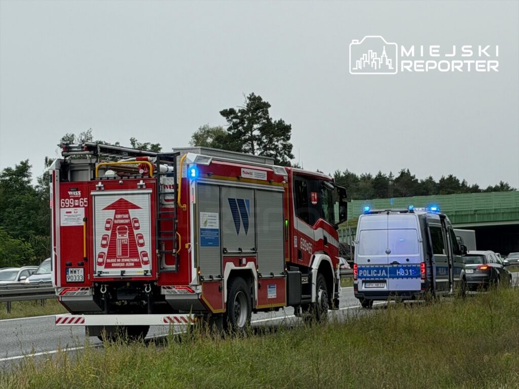 Czerwony wóz strażacki i policyjny van z włączonymi sygnałami świetlnymi zatrzymane przy drodze ekspresowej.