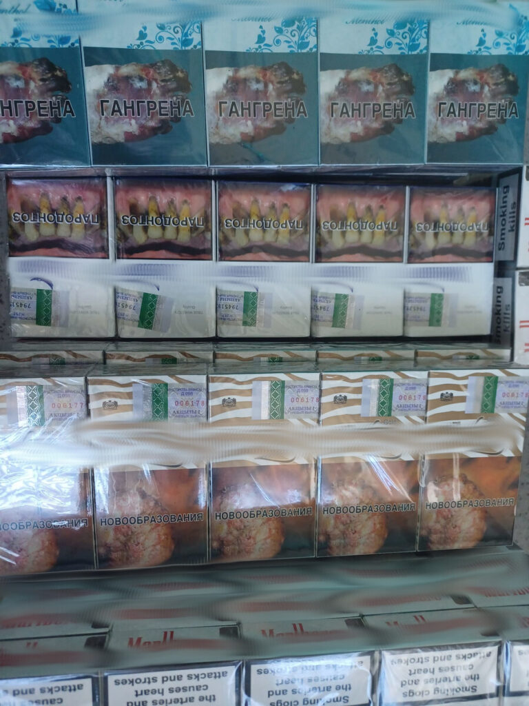 Paczki papierosów z różnymi nazwami i grafikami umieszczone na półce w sklepie.