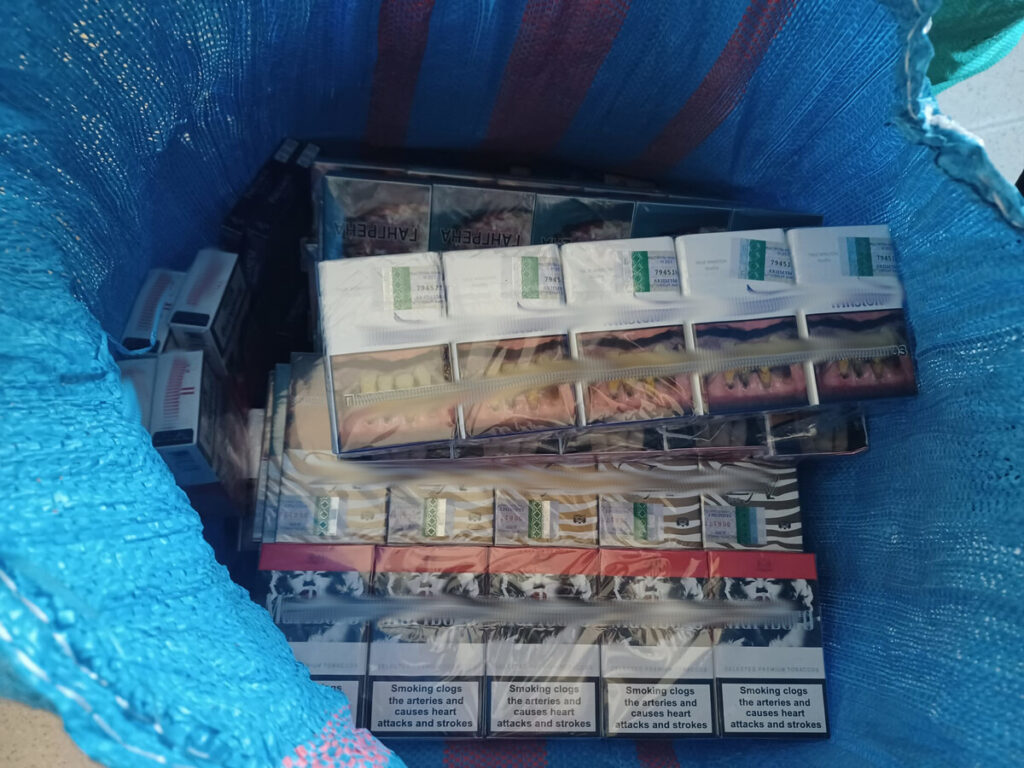 W niebieskiej torbie znajdują się paczki papierosów, w tym z widocznymi ostrzeżeniami zdrowotnymi.