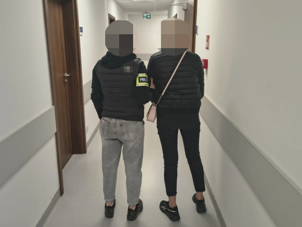 Dwóch zatrzymanych idzie korytarzem w budynku, jeden z nich ma na sobie kurtkę z napisem "POLICJA".