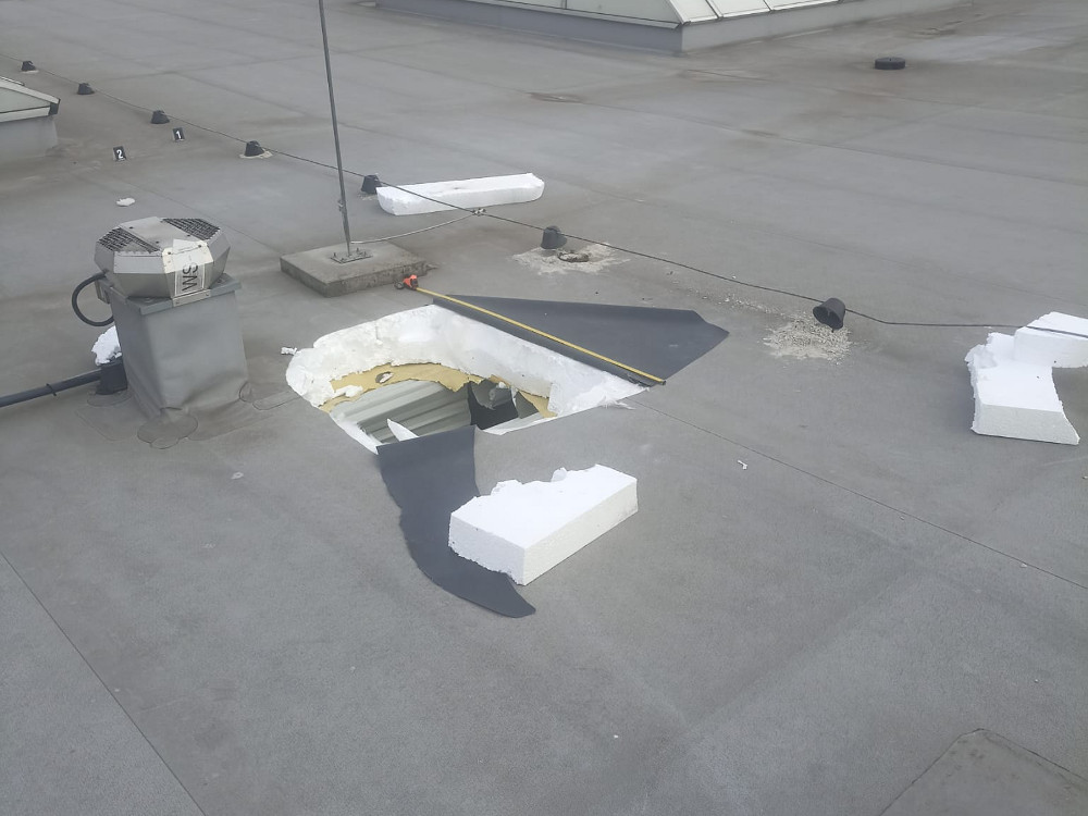 Na dachu widać otwór z usuniętą częścią pokrycia, obok wentylator i fragmenty materiałów budowlanych.