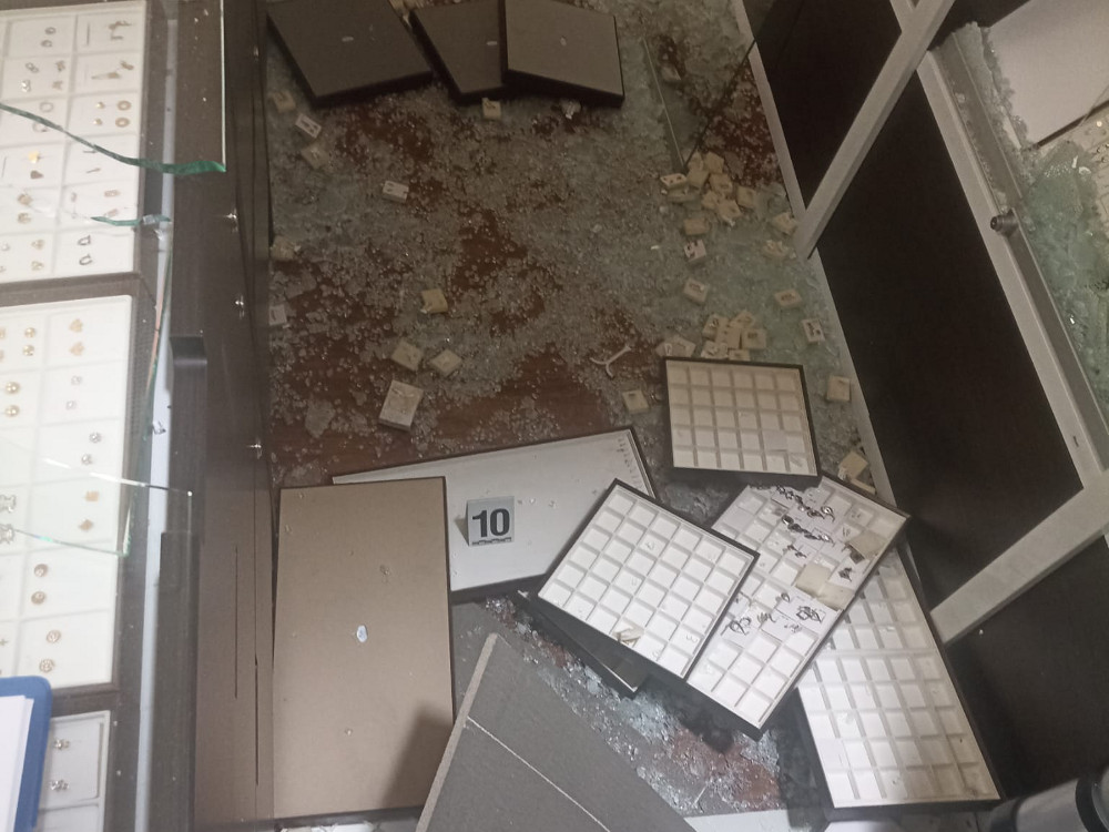 Rozbite witryny jubilerskie z porozrzucanymi elementami biżuterii i szkłem na podłodze.