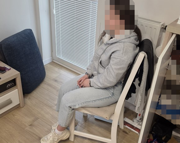 Kobieta w szarej bluzie siedzi na krześle w jasnym pomieszczeniu obok okna.