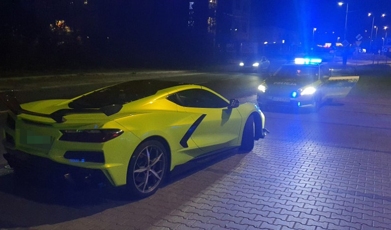 Żółty sportowy samochód stoi nocą przy drodze, a za nim znajduje się radiowóz z włączonymi niebieskimi światłami.