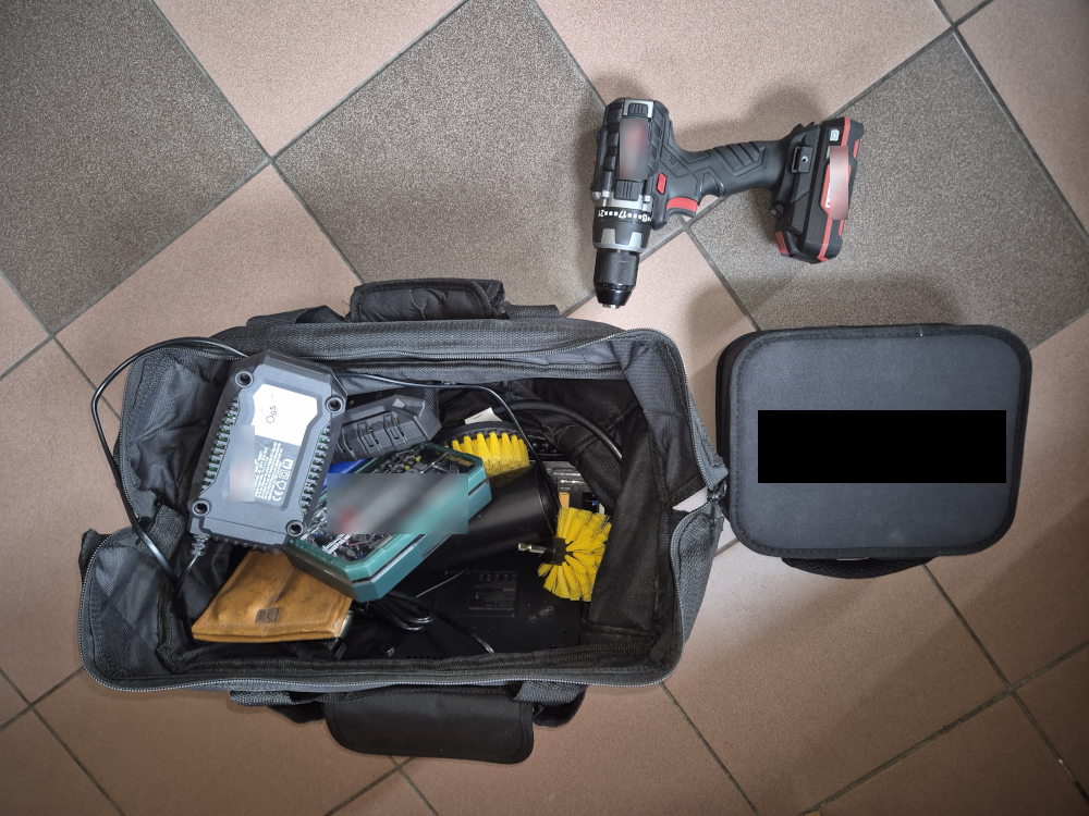 Wiertarko-wkrętarka akumulatorowa leży obok otwartej torby z elektronarzędziami i akcesoriami na kafelkowej podłodze.