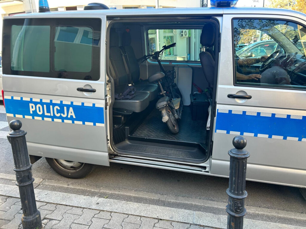 Policyjny samochód z otwartymi drzwiami, w środku stoi mały rower elektryczny na podłodze.