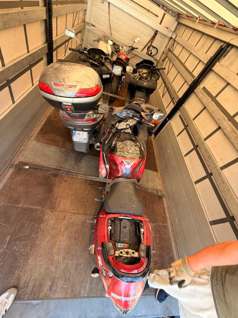 Cztery motocykle zaparkowane w przyczepie transportowej, w tym jeden z odsłoniętym siedzeniem.