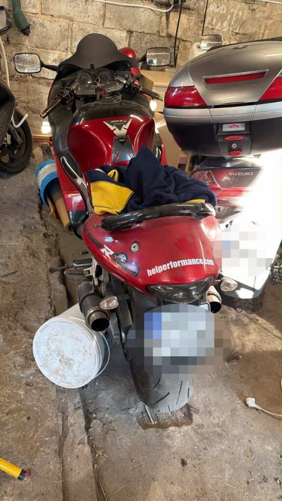 Czerwony motocykl sportowy zaparkowany w garażu, obłożony ręcznikami i z wiadrem obok.
