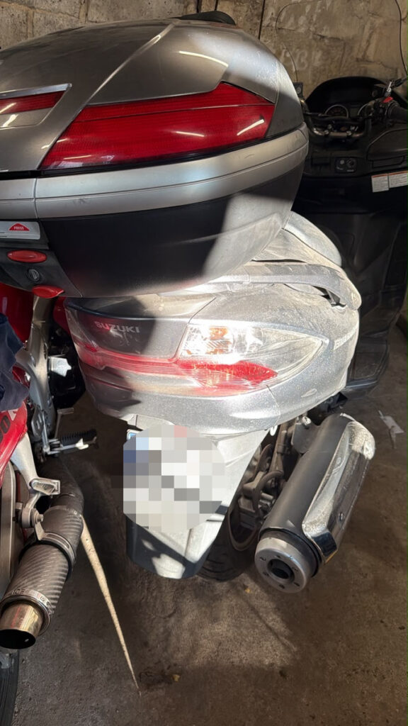 Motocykl marki Suzuki z bagażnikiem umieszczonym z tyłu, stojący w warsztacie z widocznymi śladami kurzu.