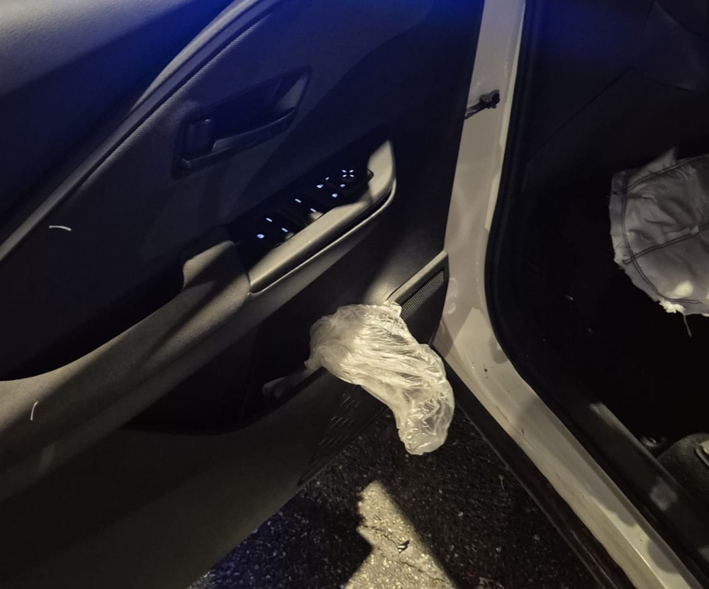 Wnętrze samochodu z widocznym plastikowym workiem zawieszonym na drzwiach oraz przyciskami sterującymi szybami.