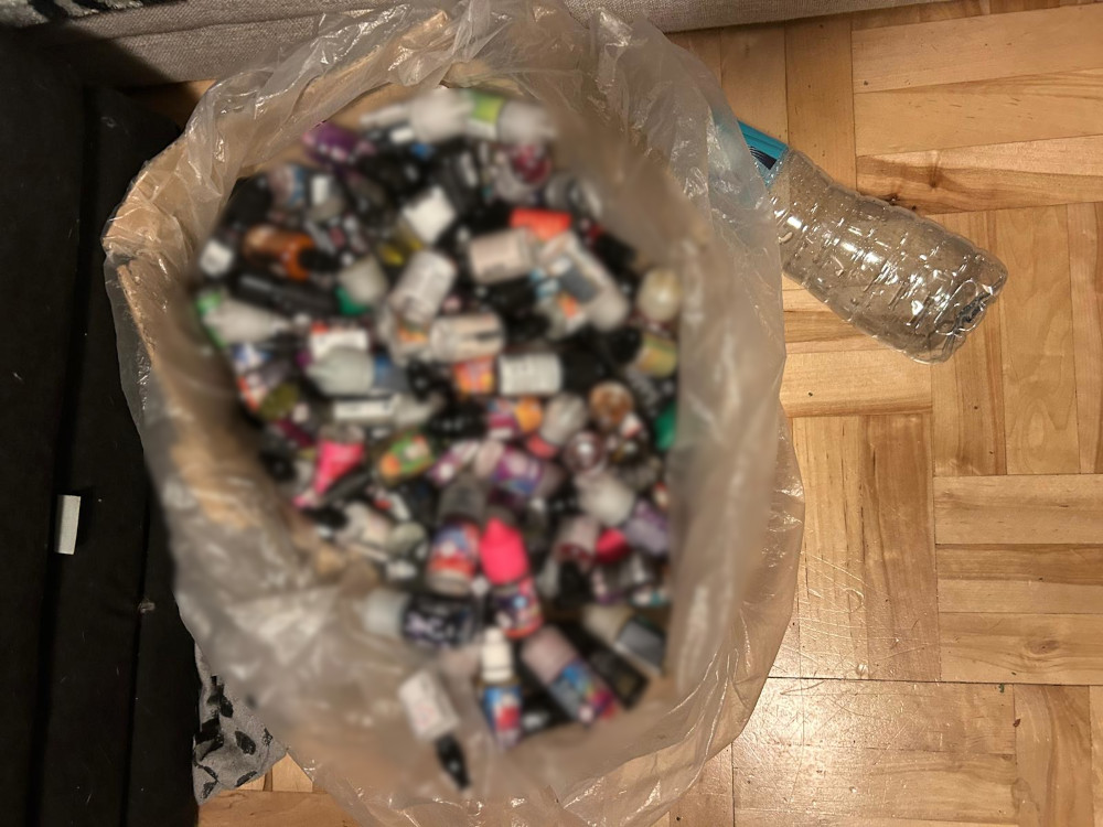 Worek z różnokolorowymi butelkami po e-liquidach leży na podłodze obok plastikowej butelki.