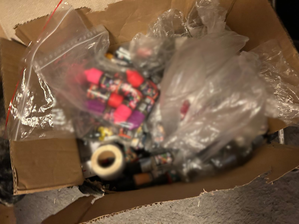 Kartonowe pudełko wypełnione kolorowymi butelkami z farbami i plastikowymi woreczkami.