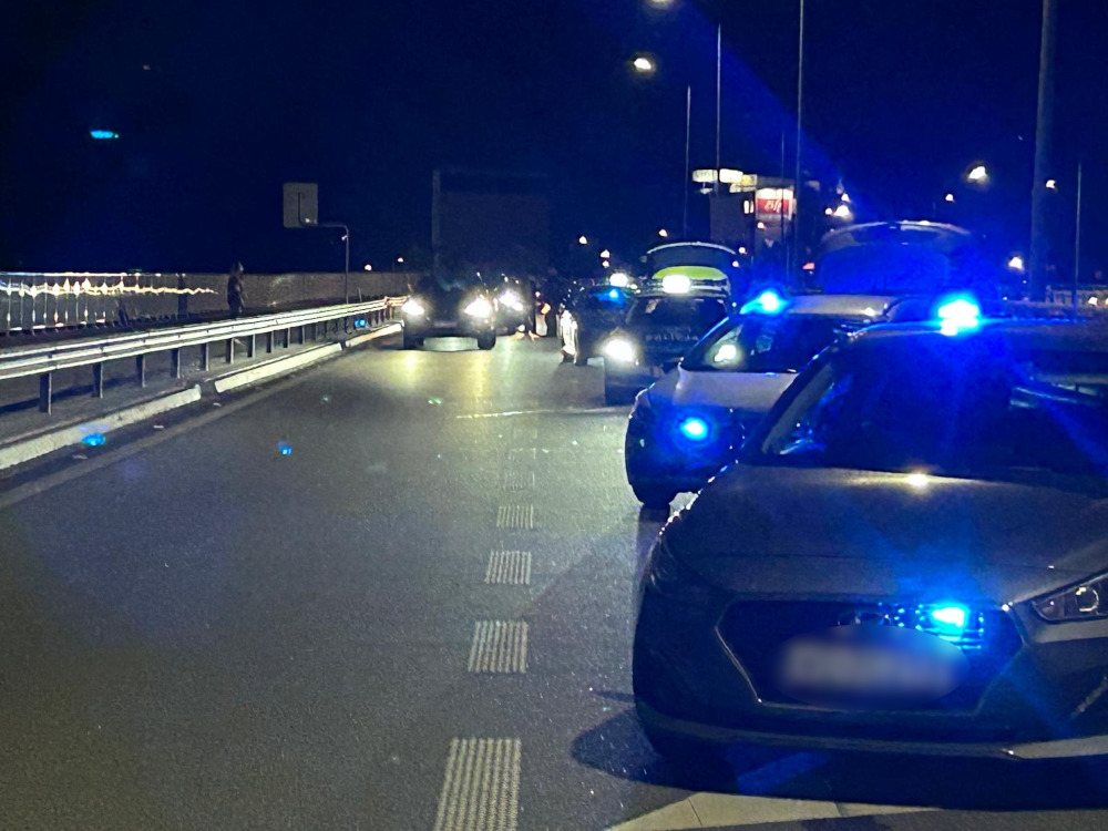 Na jezdni nocą zatrzymane są pojazdy policyjne z włączonymi niebieskimi sygnałami świetlnymi.