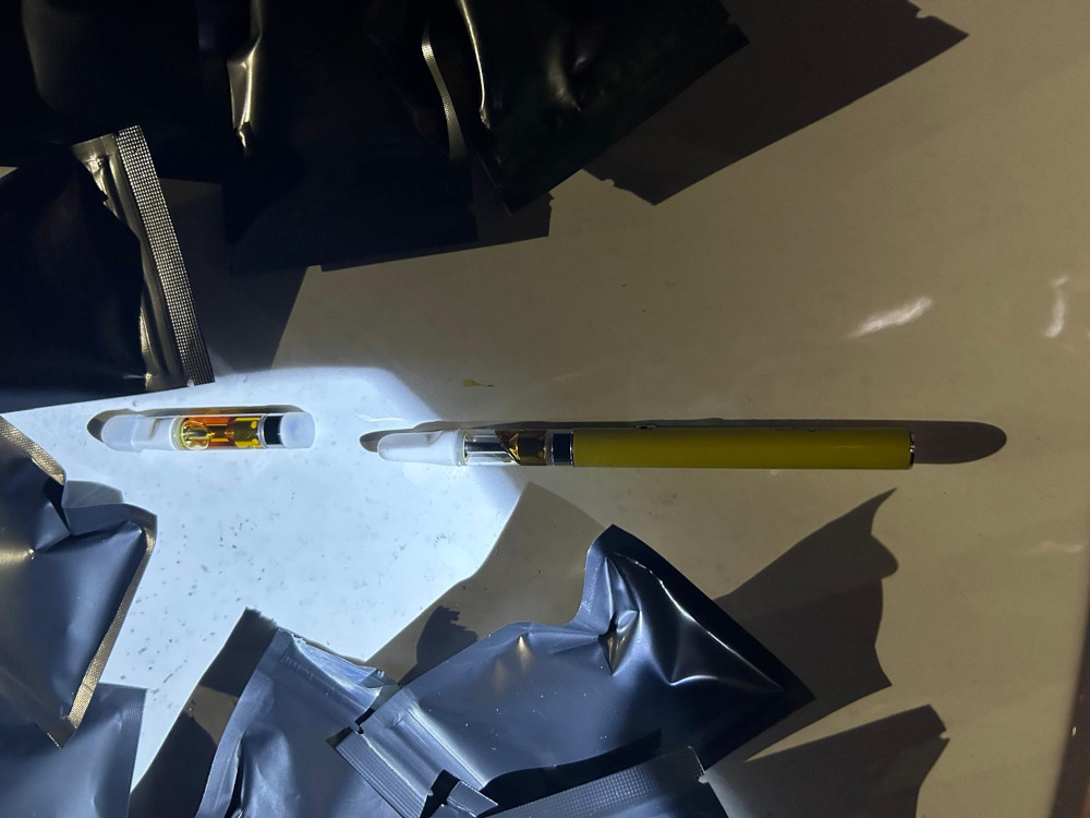 Na jasnym blacie leży żółty vaporizator obok dwóch przezroczystych kartridży z cieczą oraz czarnych, zamkniętych opakowań.