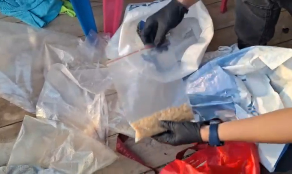 Osoba w rękawiczkach trzyma worek strunowy z zawartością, stojąc na drewnianej powierzchni otoczonej plastikowymi torbami.
