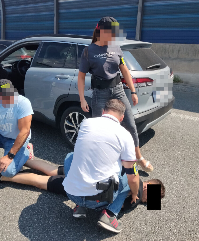 Funkcjonariusze w mundurach zatrzymują mężczyznę na drodze, obok stoi samochód osobowy.
