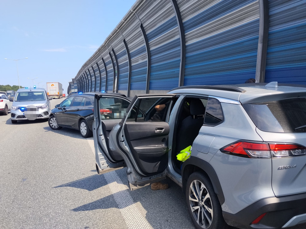 Policyjne samochody zatrzymane na autostradzie, obok otwartych drzwi szarego SUV-a, z niebieskimi światłami włączonymi.