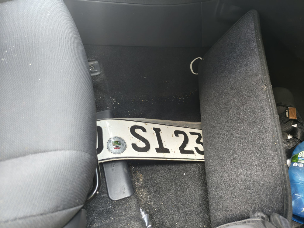 Wnętrze samochodu z widoczną tablicą rejestracyjną leżącą na podłodze obok fotela.