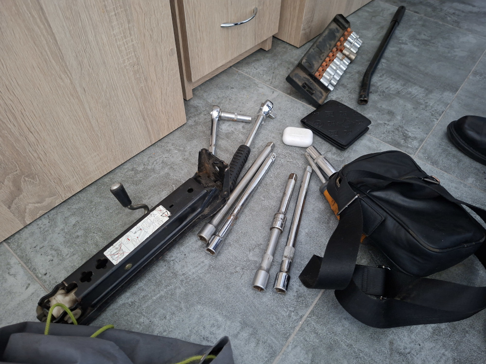 Narzędzia mechaniczne, w tym klucze nasadowe i podnośnik, rozłożone na podłodze w pomieszczeniu.