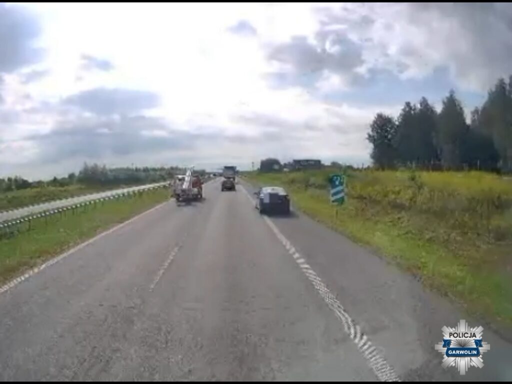 Na drodze S17 widać pojazdy, w tym samochód z przyczepą, na tle zielonej trawy i chmur.