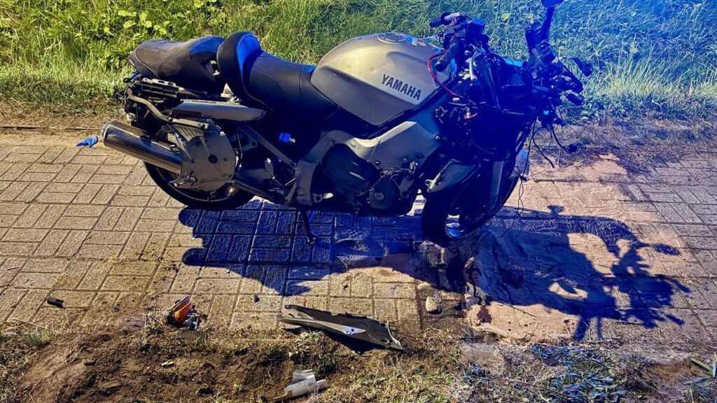 Motocykl marki Yamaha leży na poboczu drogi, obok widać uszkodzone elementy i ślady na nawierzchni.