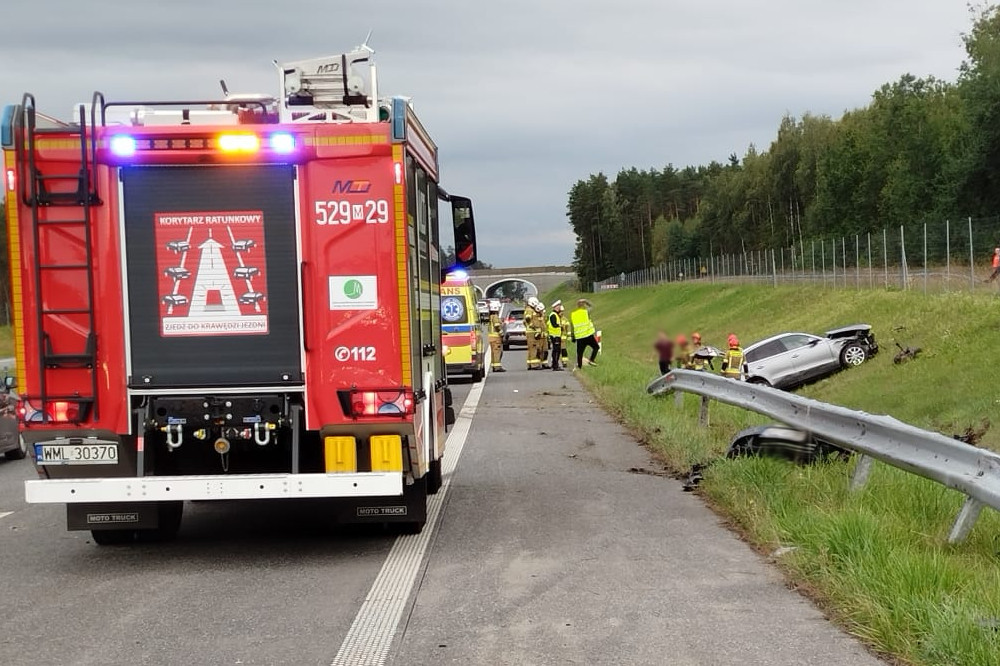 Wielu ratowników pracuje przy wypadku drogowym na poboczu drogi, obok uszkodzonego samochodu.