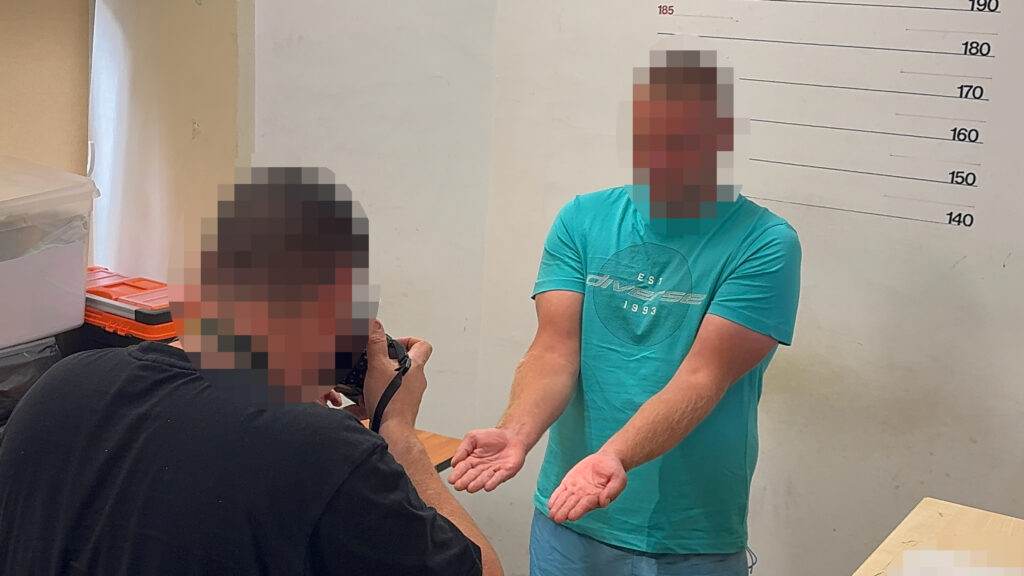 Mężczyzna w niebieskiej koszulce stoi z rękami wyciągniętymi przed siebie, podczas gdy inny mężczyzna robi mu zdjęcie.