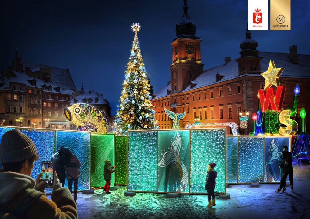 Osoby podziwiają iluminacje świąteczne na placu, obok dużej choinki i kolorowych dekoracji.