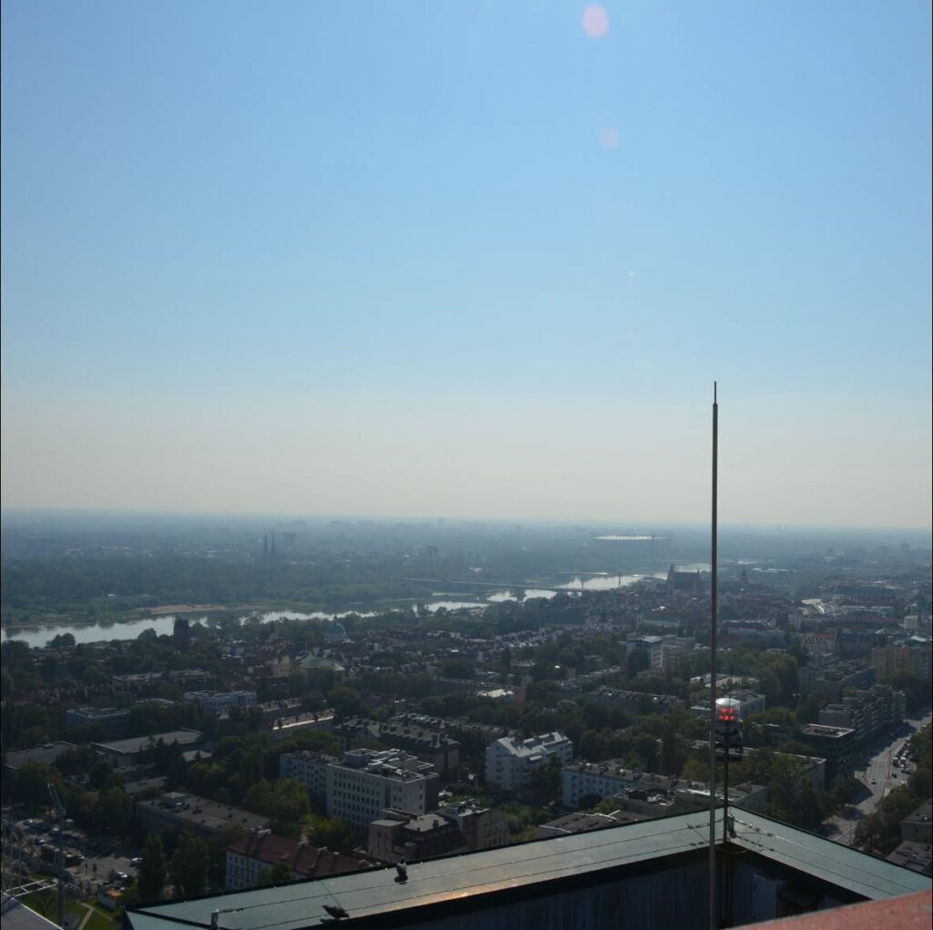 Widok z wysokości na rozległą panoramę miasta, z rzeką i zielonymi terenami w tle.