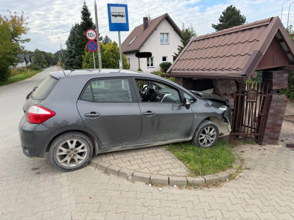 Samochód osobowy wjeżdża w murowaną wiatę śmietnikową na rogu ulicy, uszkadzając jej konstrukcję.
