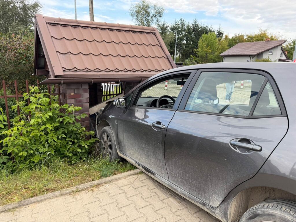 Samochód osobowy wjeżdża w murowaną wiatę śmietnikową, uszkadzając jej konstrukcję w otoczeniu zieleni.