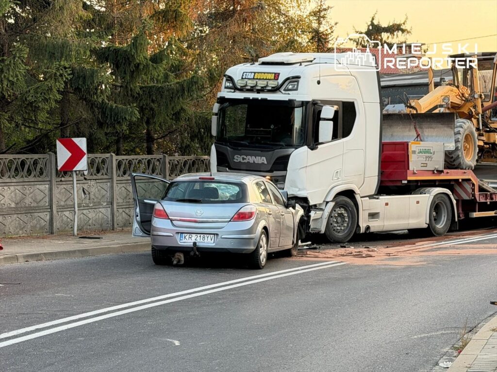 Wielka ciężarówka z uszkodzoną kabiną zderzyła się z osobowym autem na drodze, obok rosnących drzew.