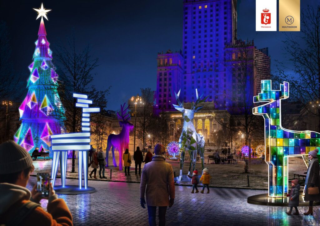 Kolorowa choinka i świetlne renifery ozdabiają nocny park, w którym spacerują ludzie, podziwiając iluminacje.
