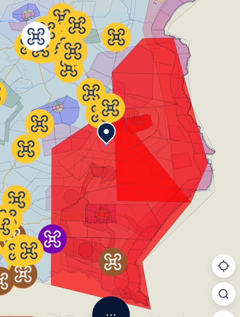 Mapa z oznaczeniami stref do lotów dronami, z czerwonym obszarem zakazu oraz ikonami dronów w różnych kolorach.