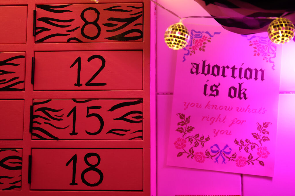 Różowa ulotka z napisem „abortion is ok” wisi obok czerwonej tablicy z numerami 8, 12, 15 i 18.
