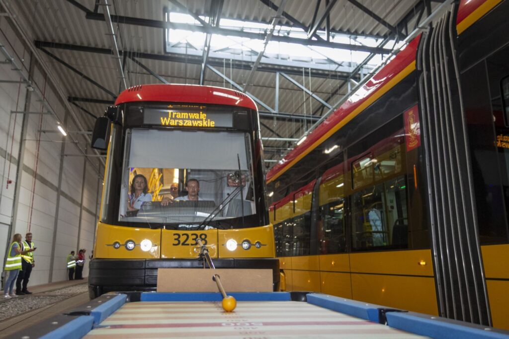 Tramwaj Warszawski z numerem 3238 stoi na torach w nowoczesnym zajezdni, a pasażerowie siedzą w kabinie.