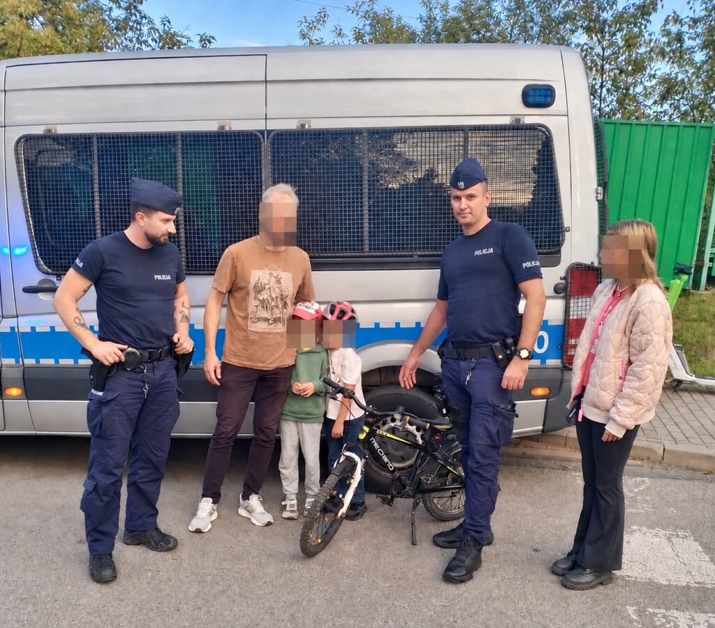 Czworo ludzi, w tym dwóch policjantów, stoi obok policyjnego vana; dzieci trzymają rower.