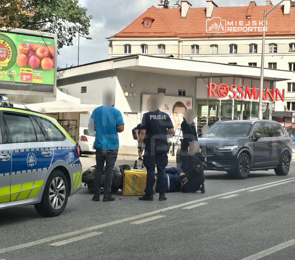 Policjanci udzielają pomocy mężczyźnie leżącemu na jezdni obok samochodu dostawczego w pobliżu sklepu Rossmann.
