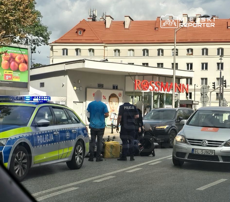 Policjanci rozmawiają z mężczyzną przy wjeździe do sklepu Rossmann, obok zaparkowane samochody.