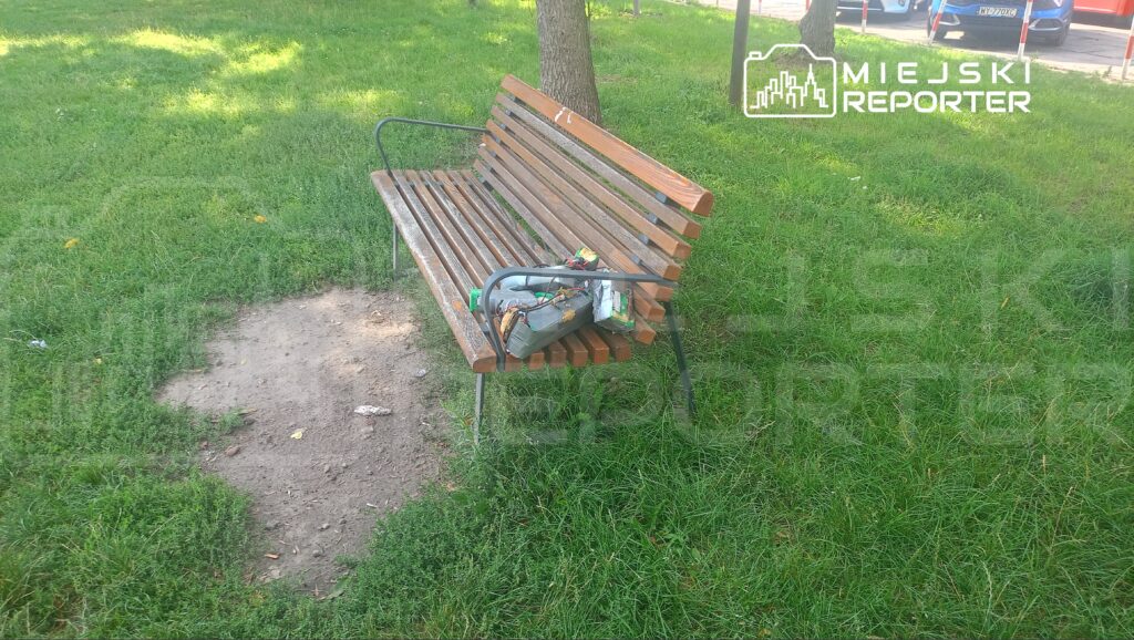 Na ławce w parku leży torba z narzędziami, otoczona zielonym trawnikiem.