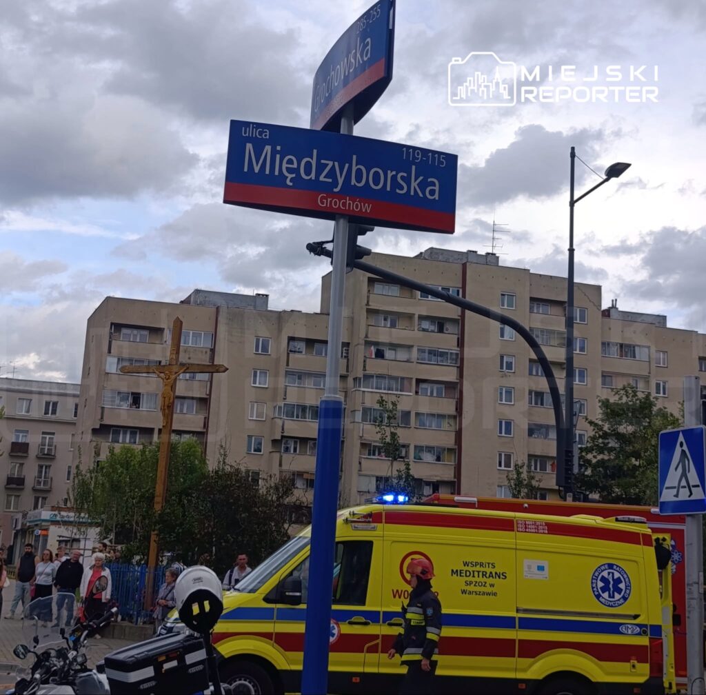 Na ulicy Międzyborskiej w Grochowie stoi ambulans z włączonymi sygnałami świetlnymi, obok grupka przechodniów.