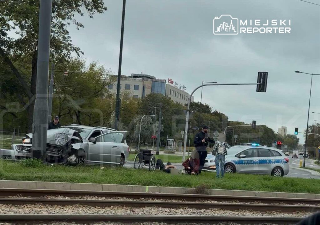 Wypadek drogowy z udziałem samochodu osobowego, obok którego z pomocą są funkcjonariusze policji oraz poszkodowani.