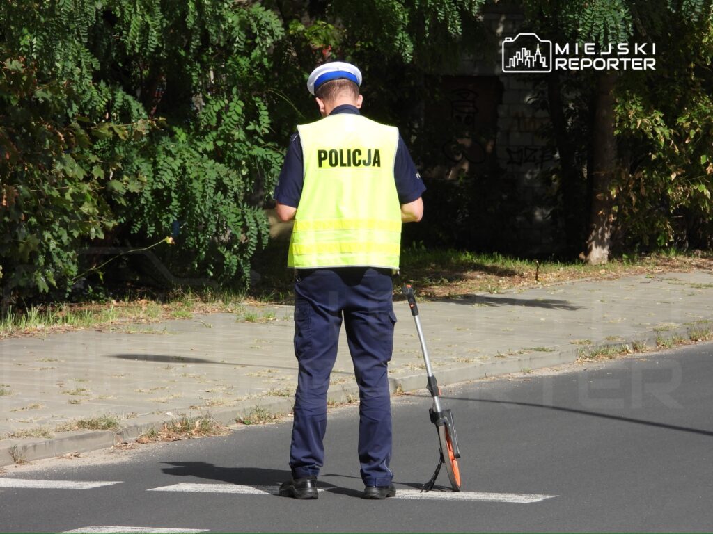 Policjant w kamizelce odblaskowej mierzy odległość na drodze przy użyciu miernika.